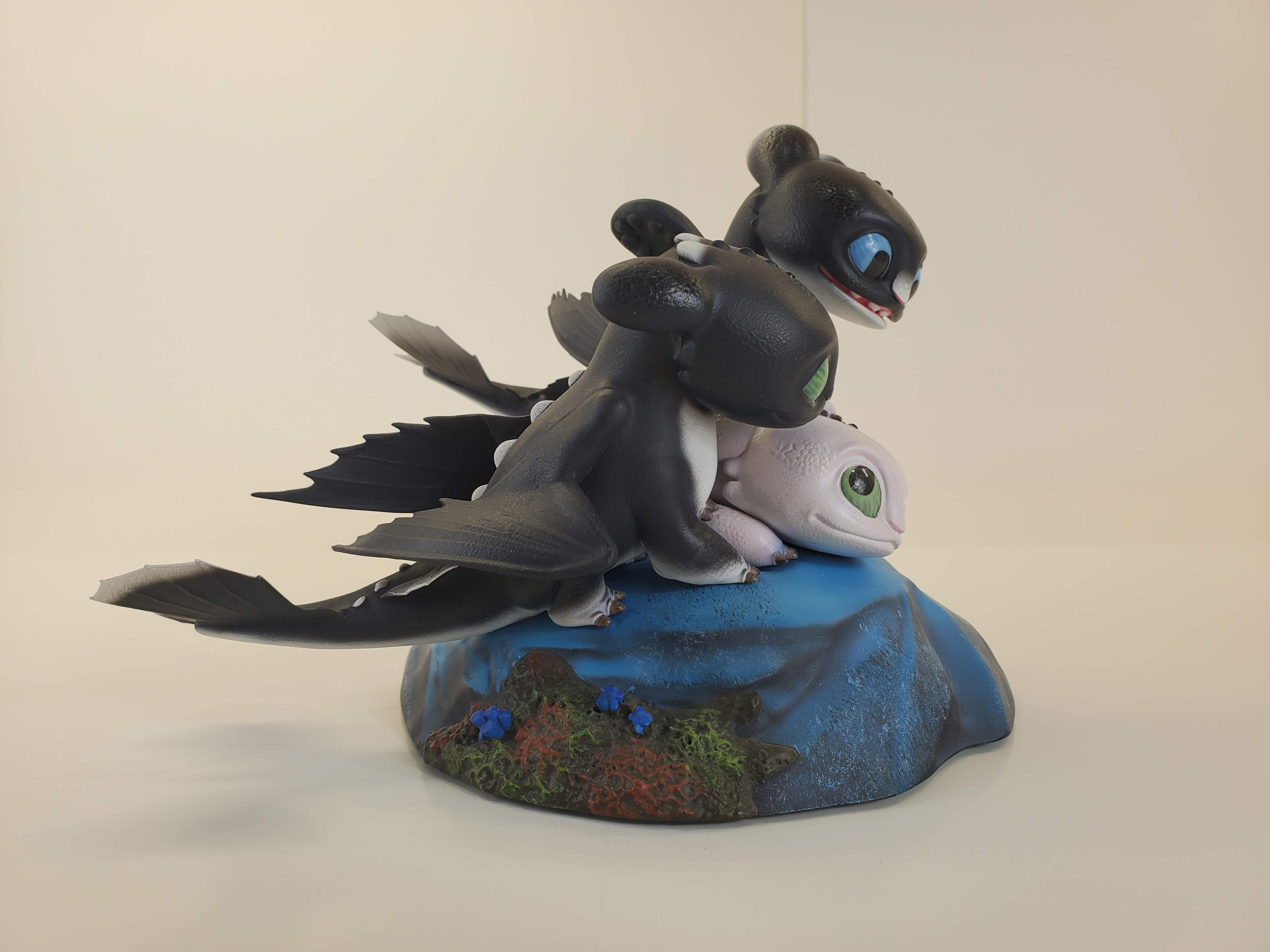 Statue of Dart, Pouncer, and Ruffrunner playfully tumbling on a blue rocky base with colorful flora.